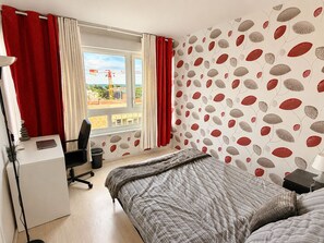 A bedroom with a bed, a desk, a chair, and a window with curtains. - Spacious, bright apartment with a balcony, 4 bedrooms (Mont-Saint-Aignan)