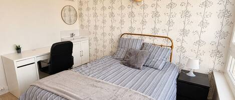 A bedroom with a bed, a desk, a chair, a nightstand, and a lamp.