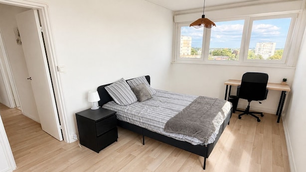 A bedroom with a bed, bedside table, lamp, desk, chair, and a view of buildings through the window. - Spacious, bright apartment with a balcony, 4 bedrooms (Mont-Saint-Aignan)