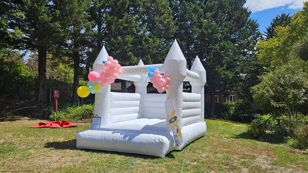 Un castillo inflable blanco con diseño de Snoopy, rodeado de árboles y césped.