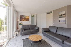A modern living room with a grey sofa, a wooden coffee table, and a painting on the wall. - Waterfront Bungalow with Garden (Makkum)