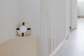 A hallway with white walls and a white floor, featuring a life preserver decoration on the wall. - Waterfront Bungalow with Garden (Makkum)
