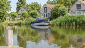 Una casa flotante atracada cerca de una zona residencial, con un cuerpo de agua tranquila que refleja los alrededores.