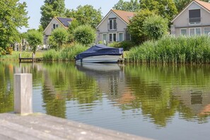 A houseboat docked near a residential area with a calm water body reflecting the surroundings. - Waterfront Bungalow with Garden (Makkum)