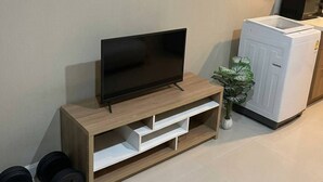 Uma sala de estar com uma TV de tela plana em um suporte de madeira, um armário branco e uma planta.
