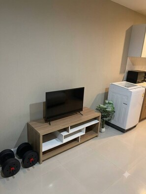 A living room with a flat-screen TV on a wooden stand, a white cabinet, and a plant. - Modern Condo Room with Private Facilities in Phasi Charoen (Phasi Charoen)