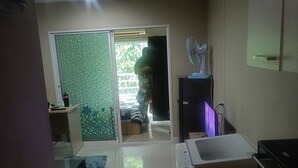 Quarto com porta de vidro deslizante para uma varanda, bancada branca com pia, ventilador e frigorífico.