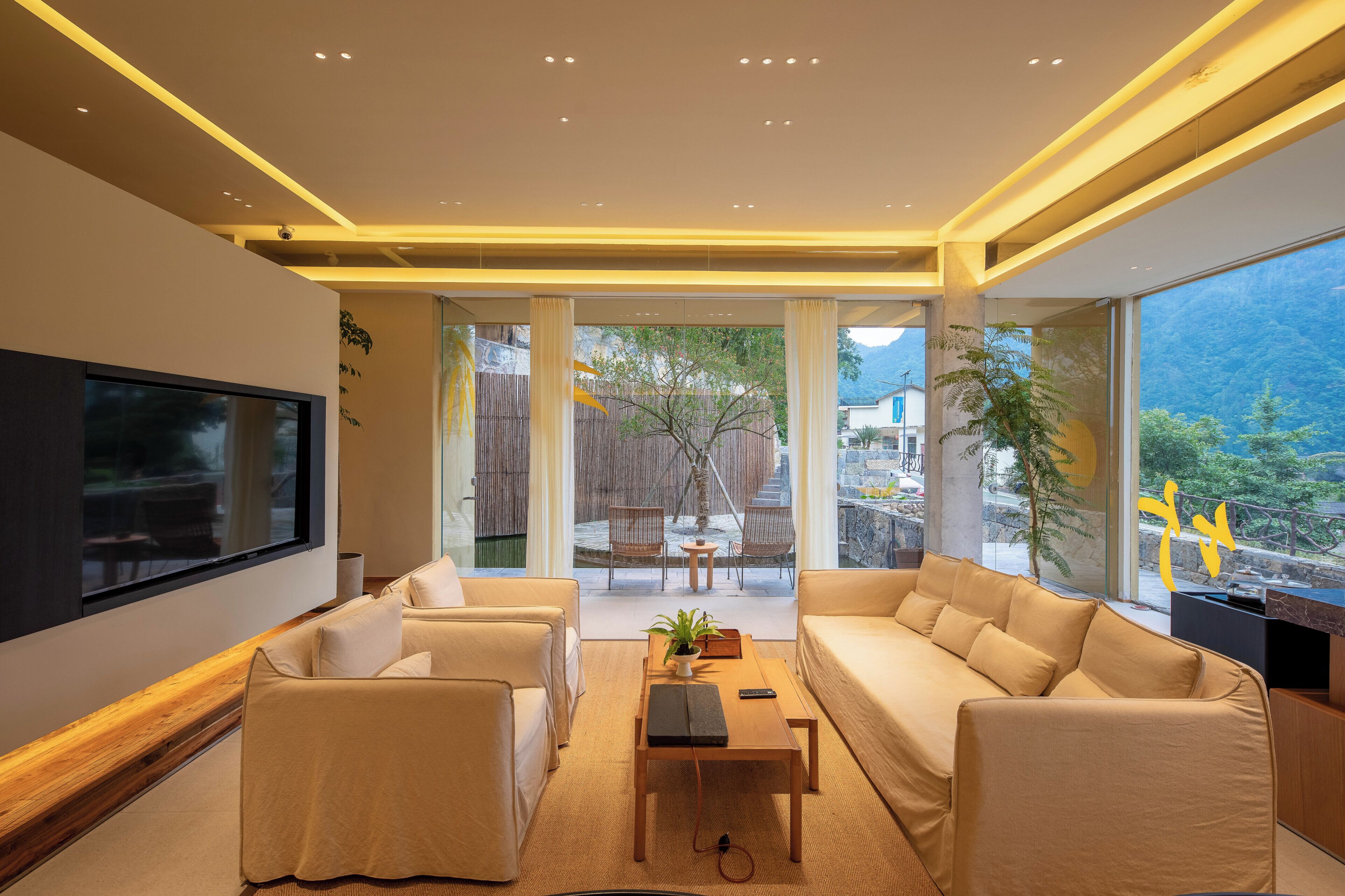 A modern living room with a flat-screen TV, comfortable seating, and a view of a mountainous landscape.