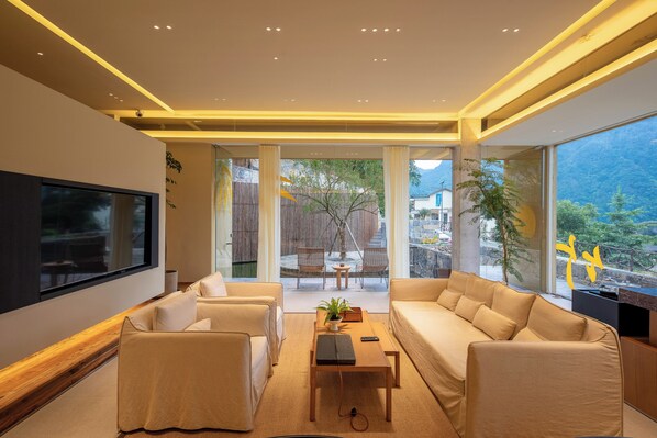 A modern living room with a flat-screen TV, comfortable seating, and a view of a mountainous landscape.