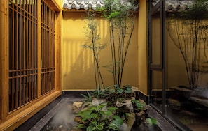 Una stanza tradizionale in stile giapponese, con pavimento in tatami, porta scorrevole in carta di riso e un piccolo giardino interno con rocce e piante.
