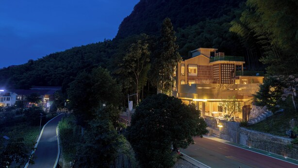 A modern building with a curved facade, surrounded by lush greenery and a mountain backdrop. - Xuzhu Avatar Mountain Hideaway (Zhangjiajie)