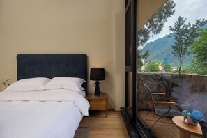 A bedroom with a bed, bedside lamp, and a view of a mountainous landscape through a large window.