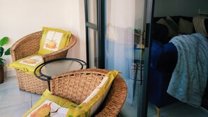 Uma varanda com móveis de vime, uma porta de vidro e vista para o interior.