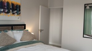 Quarto com cama, um quadro na parede, uma porta e uma janela com cortina.
