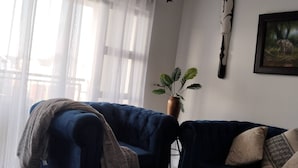 Uma sala de estar com um sofá azul, uma mesa de centro, um vaso com planta e um quadro na parede.