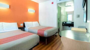 Une chambre d’hôtel avec deux lits, une petite table et une salle de bain visible à travers une porte ouverte.