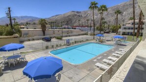 Une piscine entourée de chaises longues et de parasols, avec des palmiers et des montagnes en arrière-plan.