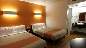 Habitación de hotel con dos camas, piso de madera, una mesita y un baño visible a través de una puerta abierta.