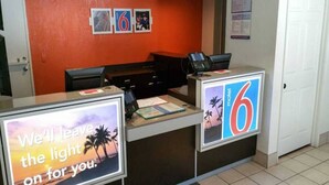 Un comptoir d’accueil d’hôtel avec un mur rouge, un écran numérique et un panneau indiquant les prix des chambres.