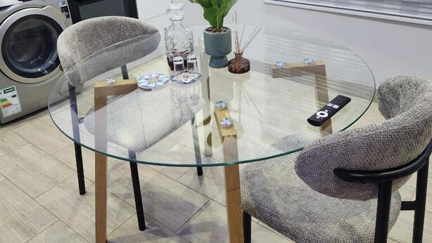A modern kitchen with a glass-top table, two chairs, a washing machine, and a potted plant. - Cozy and Modern Apartment Rental in Akasia, Pretoria (Akasia)