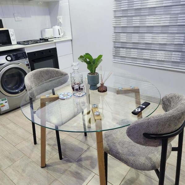 A modern kitchen with a glass-top table, two chairs, a washing machine, and a potted plant.