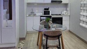 A modern kitchen with white cabinets, a glass dining table, and a built-in microwave. - Cozy and Modern Apartment Rental in Akasia, Pretoria (Akasia)