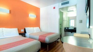 Ein Hotelzimmer mit zwei Betten, einem kleinen Tisch und einem durchgegangenen Tür angedeuteten Badezimmer.