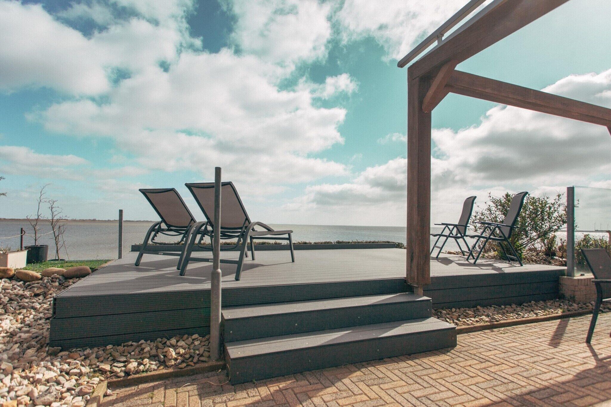 Un espace extérieur abrité, aménagé avec des sièges, et accessible par des marches menant à un point de vue sur la mer.