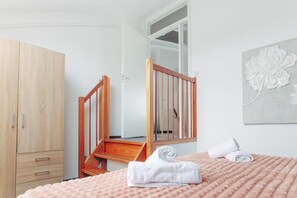 A bedroom with a wooden wardrobe, a desk, a bed with a pink blanket, and a wall-mounted decorative piece. - Deluxe Dike Villa with Sauna for 6 (Makkum)
