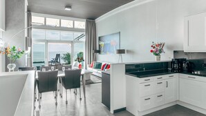 A modern kitchen with white cabinets, a dining area with a table and chairs, and a large window with a view of the sea. - Deluxe Dike Villa with Sauna for 6 (Makkum)