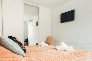 A hotel room with a bed, pillows, a flat-screen TV, and a mirror.