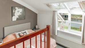 A bedroom with a bed, a nightstand, a window with a view of a bridge and greenery, and a painting on the wall. - Deluxe Dike Villa with Sauna for 6 (Makkum)
