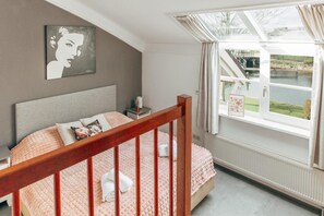 A bedroom with a bed, a nightstand, a window with a view of a bridge and greenery, and a painting on the wall. - Deluxe Dike Villa with Sauna for 6 (Makkum)