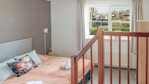 A bedroom with a bed, a window with a view of a canal, and a wooden railing. - Deluxe Dike Villa with Sauna for 6 (Makkum)