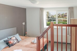 A bedroom with a bed, a window with a view of a canal, and a wooden railing. - Deluxe Dike Villa with Sauna for 6 (Makkum)