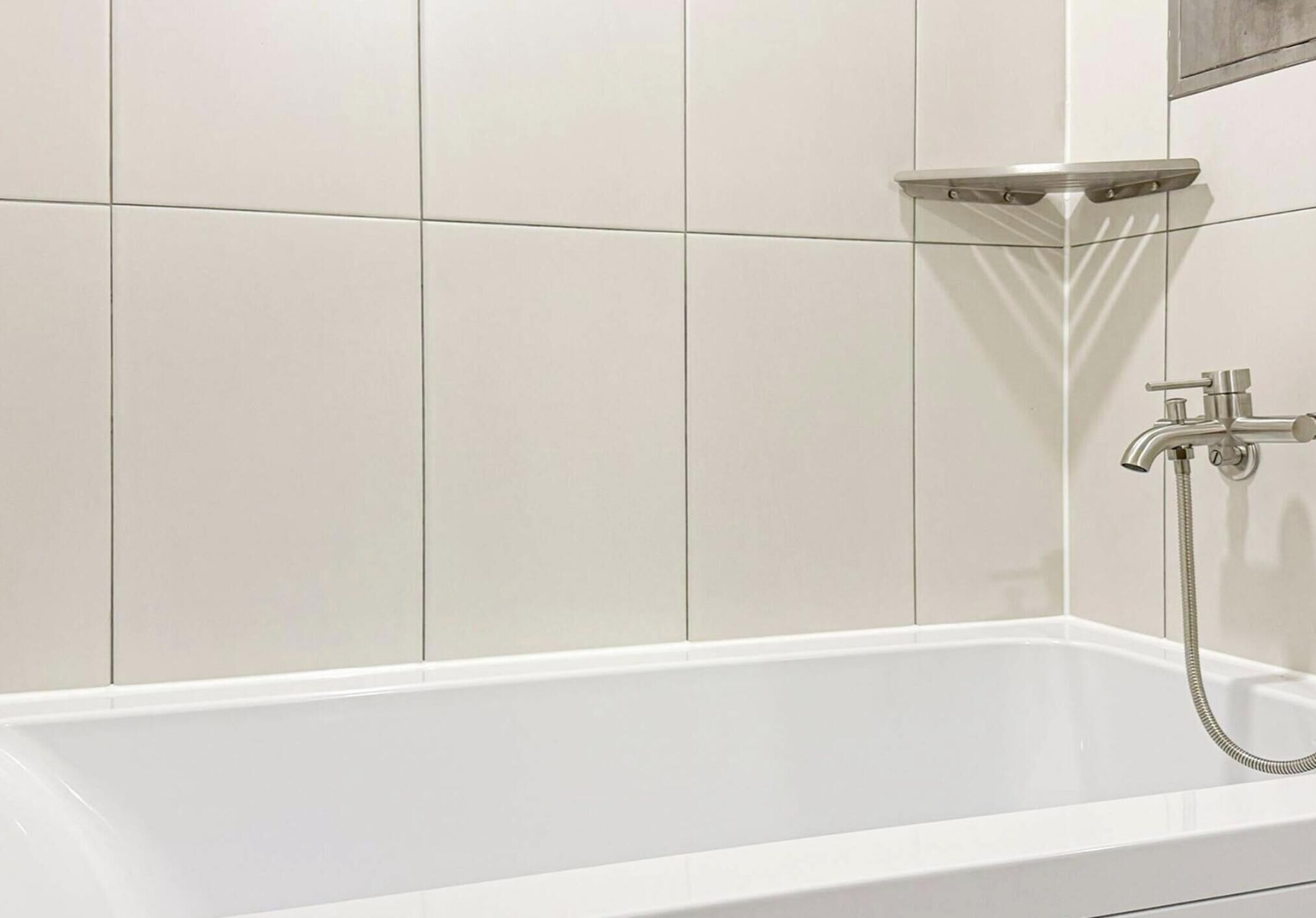Una bañera blanca con ducha de mano y grifo empotrado.