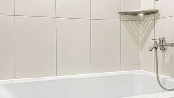 Una bañera blanca con ducha de mano y grifo empotrado.