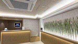A hotel reception area with a wooden reception desk, a digital display, and a wall-mounted plant display. - MH Hotel Geumam Terminal Branch No. 4 (Jeonju)