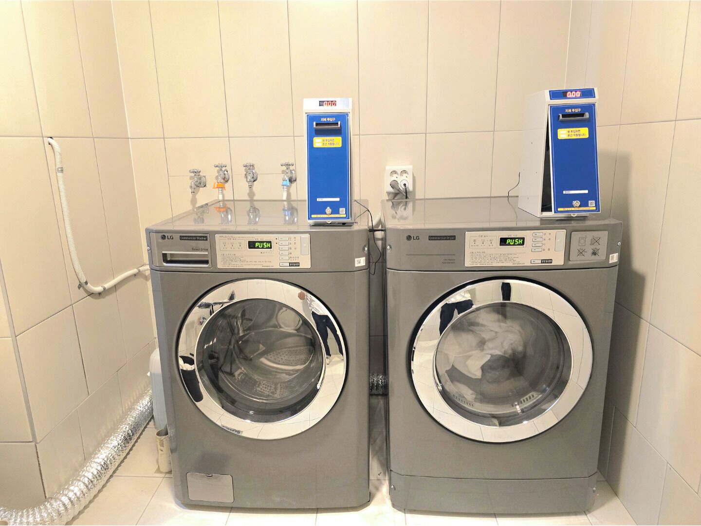 Two LG commercial washers in a tiled room with a hose connected to the left washer.