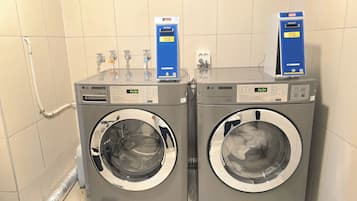 Two LG commercial washers in a tiled room with a hose connected to the left washer.