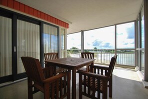 A balcony with a table and chairs, a view of a body of water, and a red wall. - IJsselmeer Apartment with Balcony (Makkum)