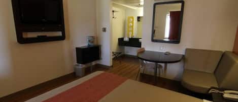 Habitación de hotel con cama, televisión, escritorio con silla, sofá y espejo.