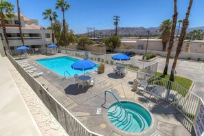 A swimming pool area with lounge chairs and umbrellas, surrounded by a fence and palm trees.