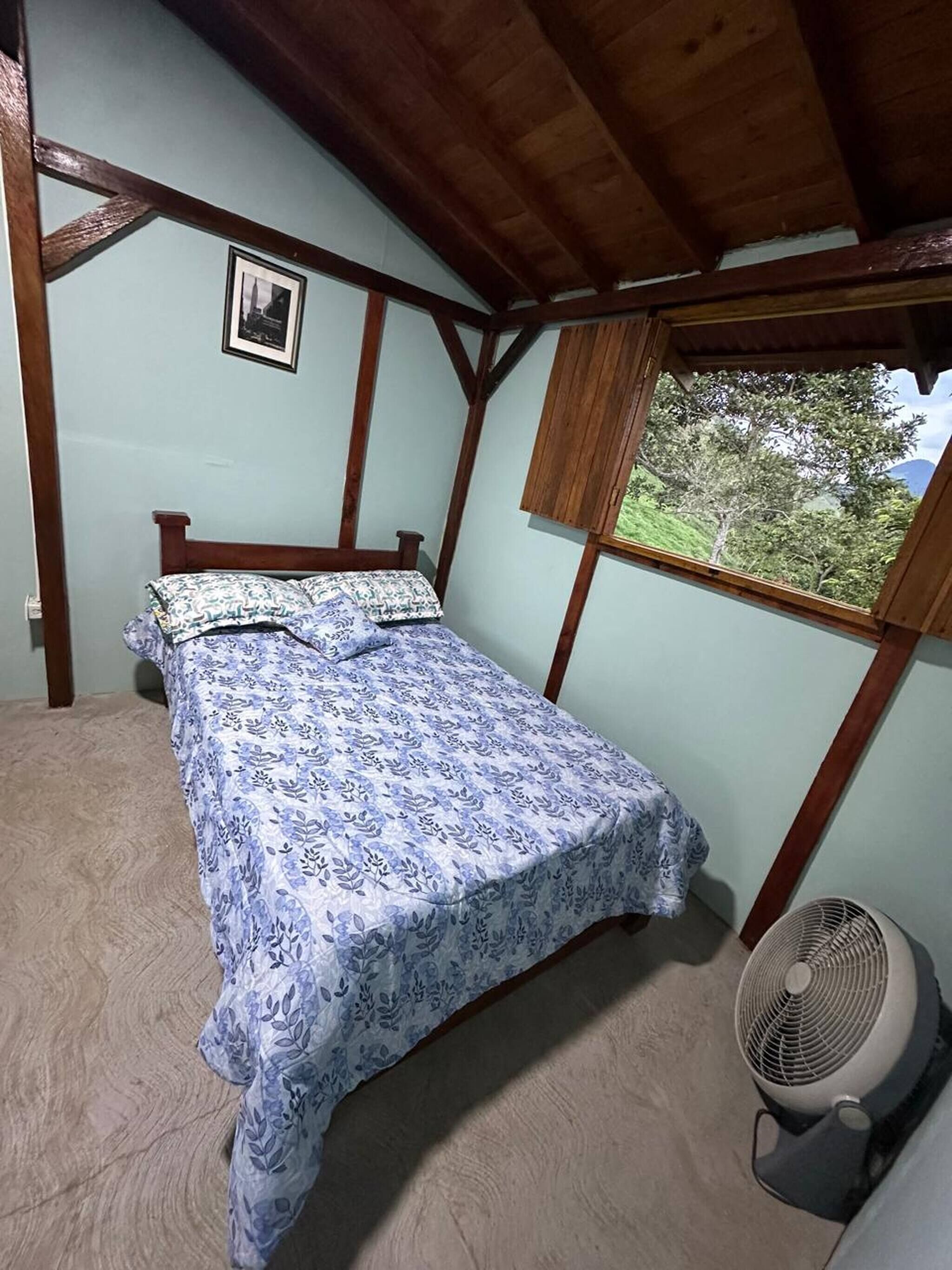 A bedroom with a bed, a window, and a fan.