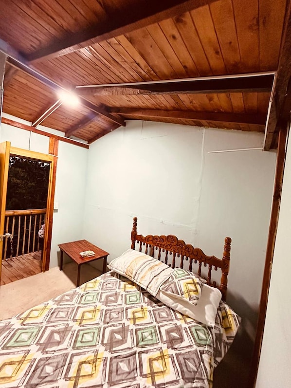 Une chambre avec un plafond en bois, un lit avec une literie à motifs, une table de chevet et une petite table.