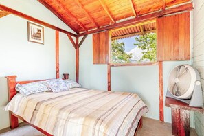 A wooden-framed room with a bed, a window, and a fan.
