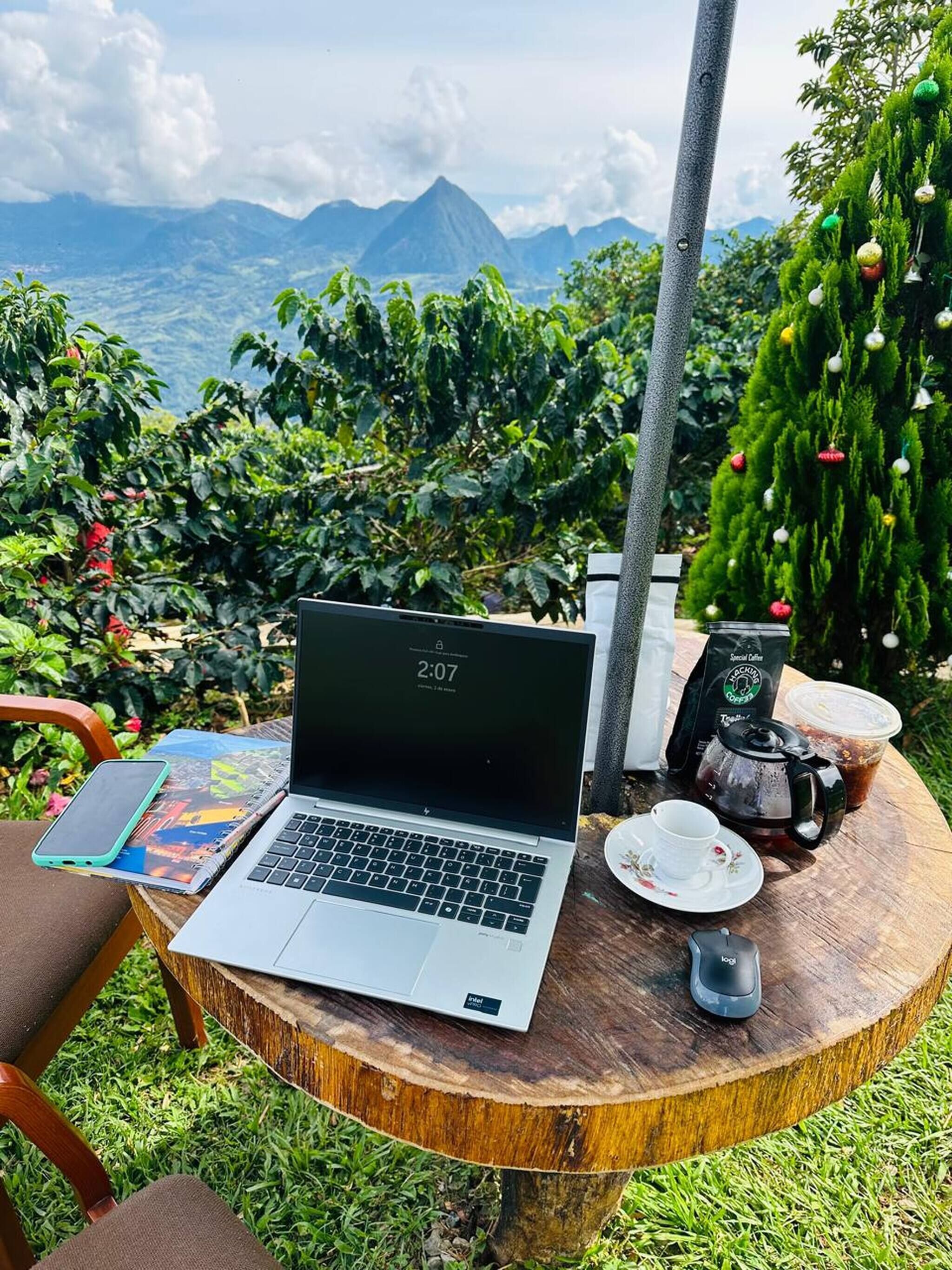 Una computadora portátil sobre una mesa de madera, con una taza de café, un paquete de café y un teléfono inteligente a un lado.