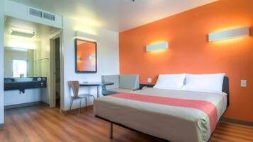 Quarto de hotel com cama, escrivaninha, cadeira e espelho.