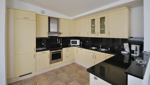 Una cocina con gabinetes de color claro, encimera negra, electrodomésticos de acero inoxidable y suelo de baldosas.