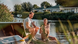A couple relaxing on a dock by a body of water, with a house in the background. - Lakeview Apartment with Dual Balconies (Makkum)
